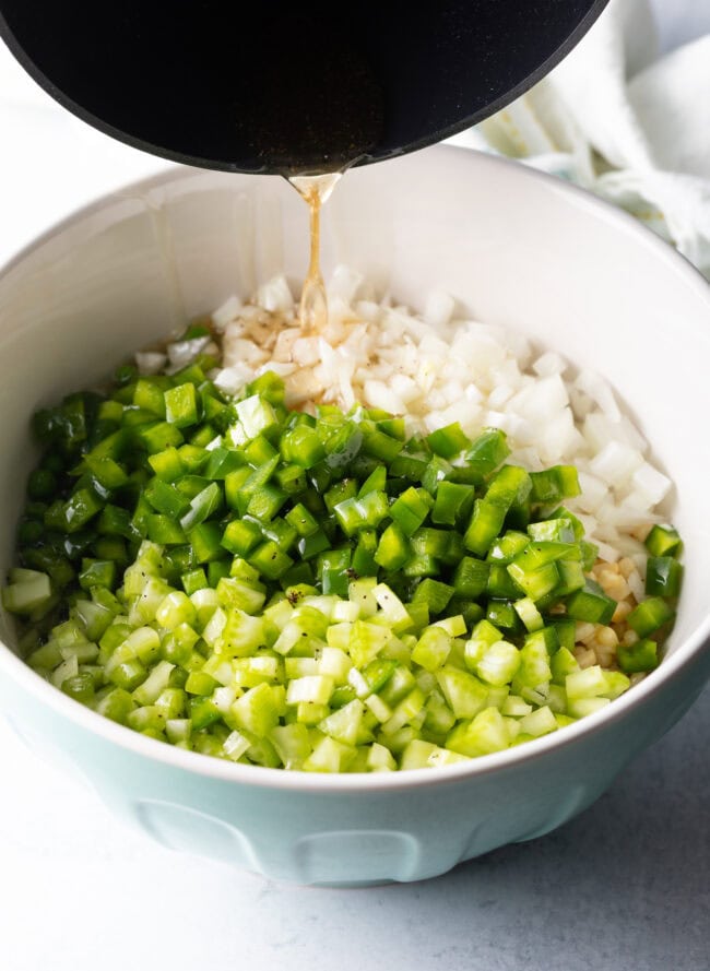 Pouring vinegar marinade over chopped veggies in a white bowl.