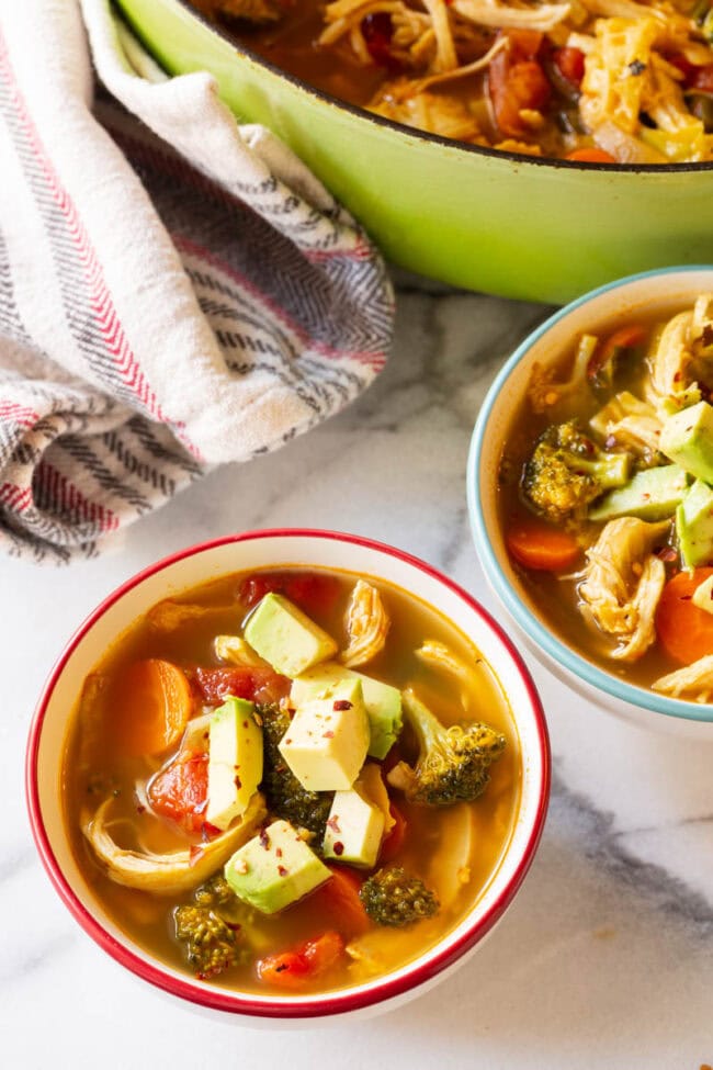 Overhead bowls of low carb chicken soup topped with avocado. 