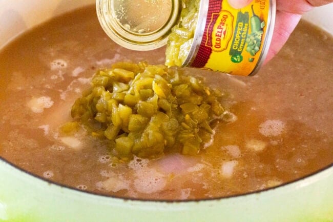 Hand pouring a can of green chiles into a pot of soup. 