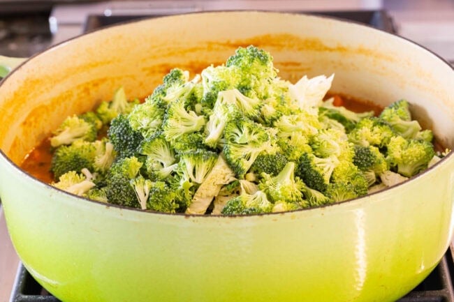 Pot of soup with fresh broccoli florets being added. 