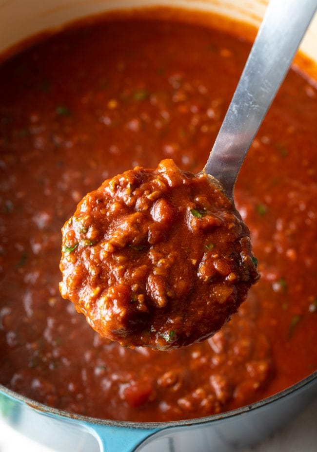 Meat sauce in a pot with a ladle scooping up a serving. 