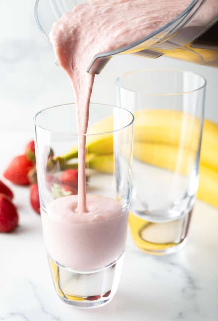 Pouring pink smoothie from a blender jar into a tall glass.