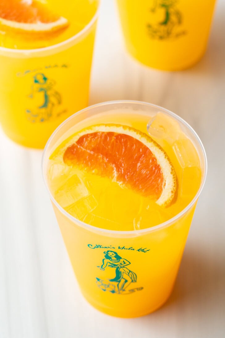 Top down view of 3 sunny d vodka seltzer drinks, each in a glass cup with slice of orange on top.