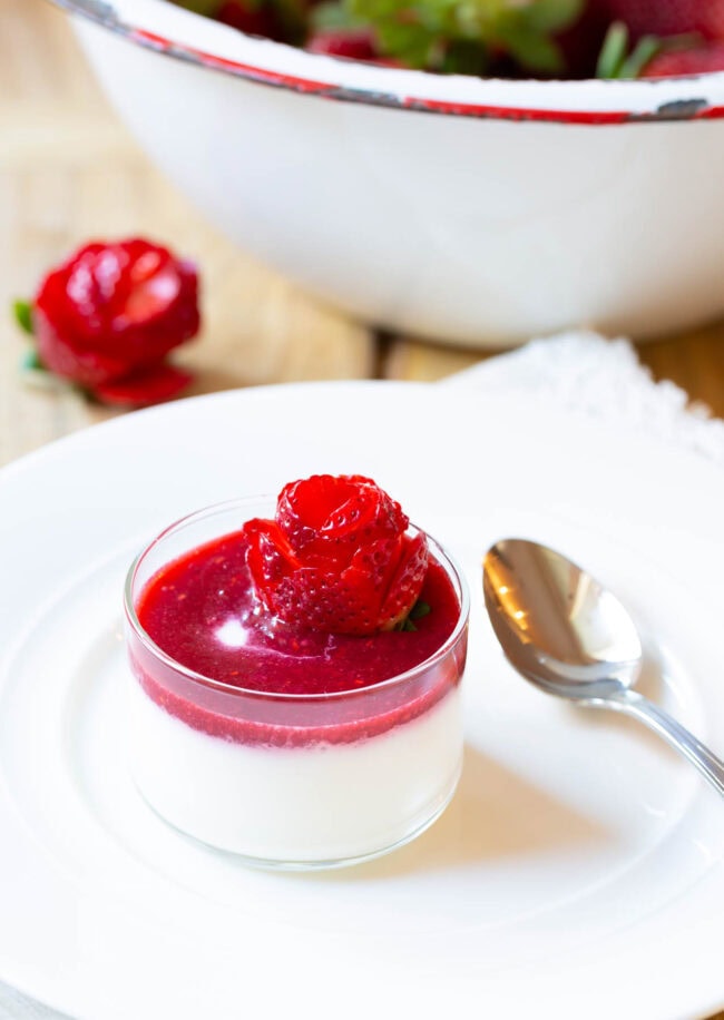 Small glass dish with silky swedish cream topped with berry compote and strawberry rose.