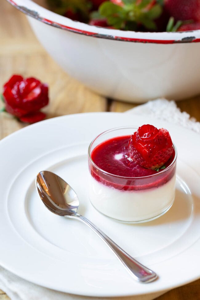 Small glass dish with silky swedish cream topped with berry compote and strawberry rose.