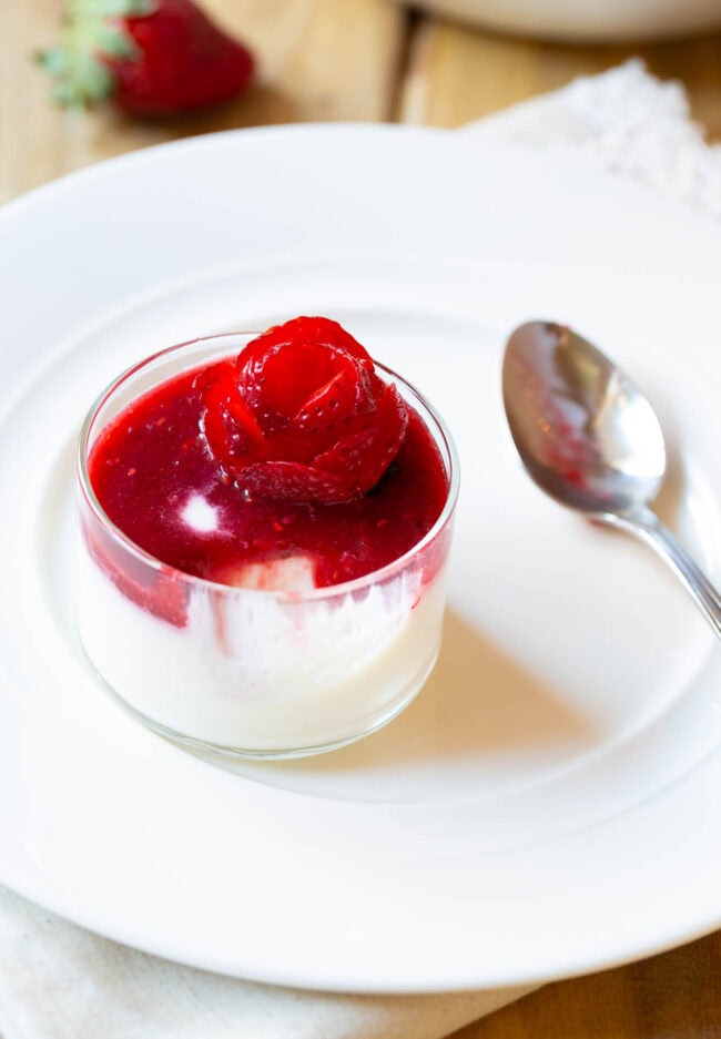 Small glass dish with silky white mixture topped with berry compote and strawberry rose.