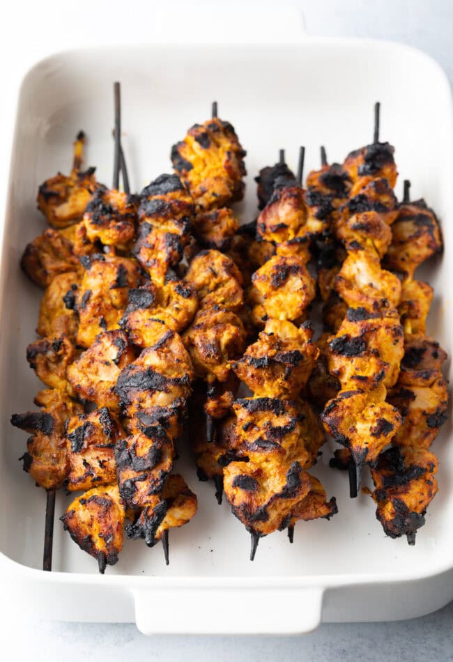 White baking dish with half a dozen tikka kabobs, grilled crisp.