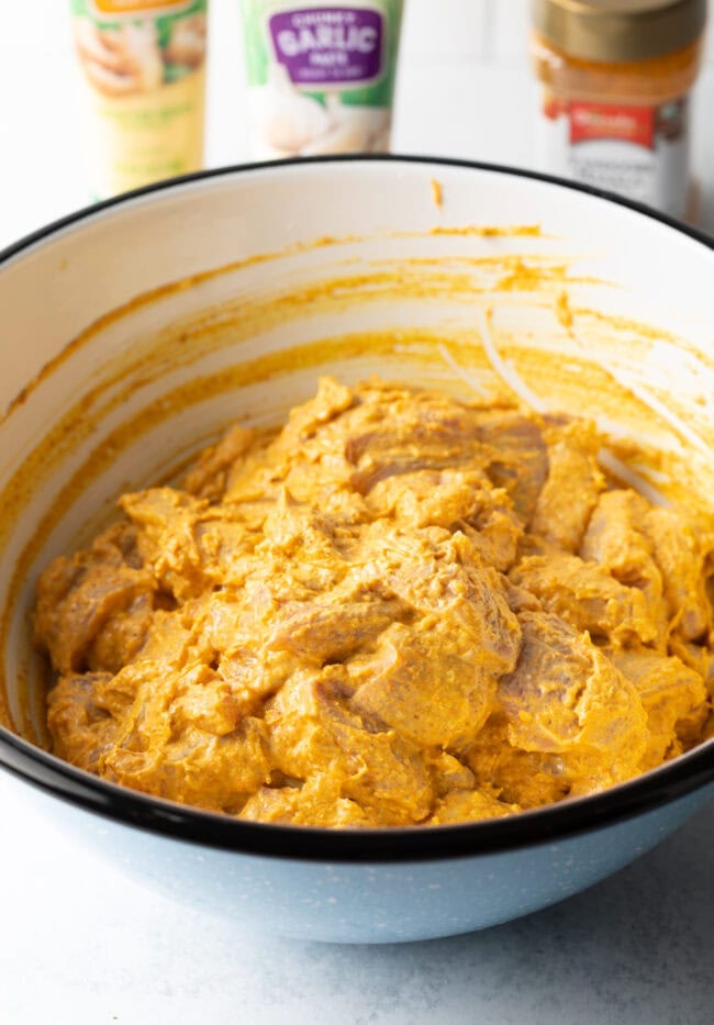 Chunks of raw chicken in a bowl each piece coated in a blend of yogurt and spices.