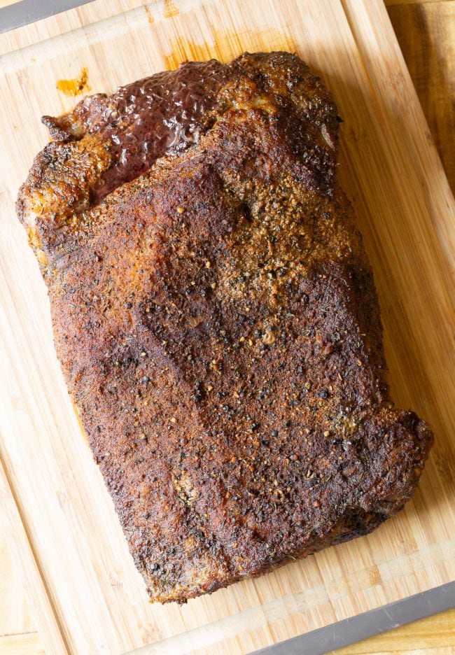 Brisket after being cooked in the oven and set on a wooden cutting board.