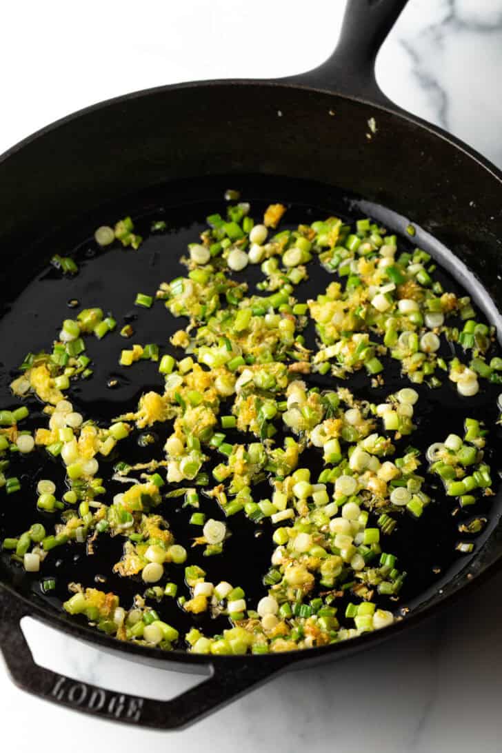 Sauteeing scallion white and grated ginger in a cast iron skillet.