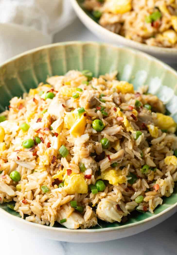 Top down view of a green plate with crab fried rice with chunks of crab meat and peas.