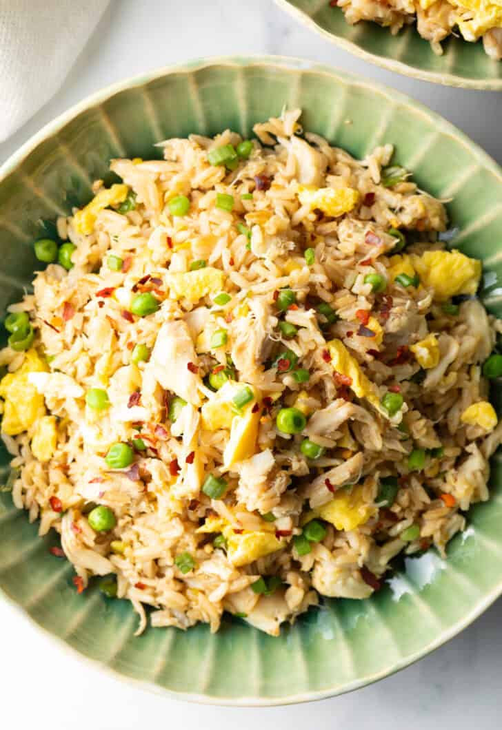 Top down view of a green plate with crab fried rice with chunks of crab meat and peas.