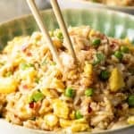 Chopsticks holding a bite of fried rice with crab, taking it from a plate of the rice.