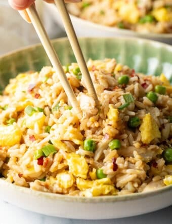 Chopsticks holding a bite of fried rice with crab, taking it from a plate of the rice.