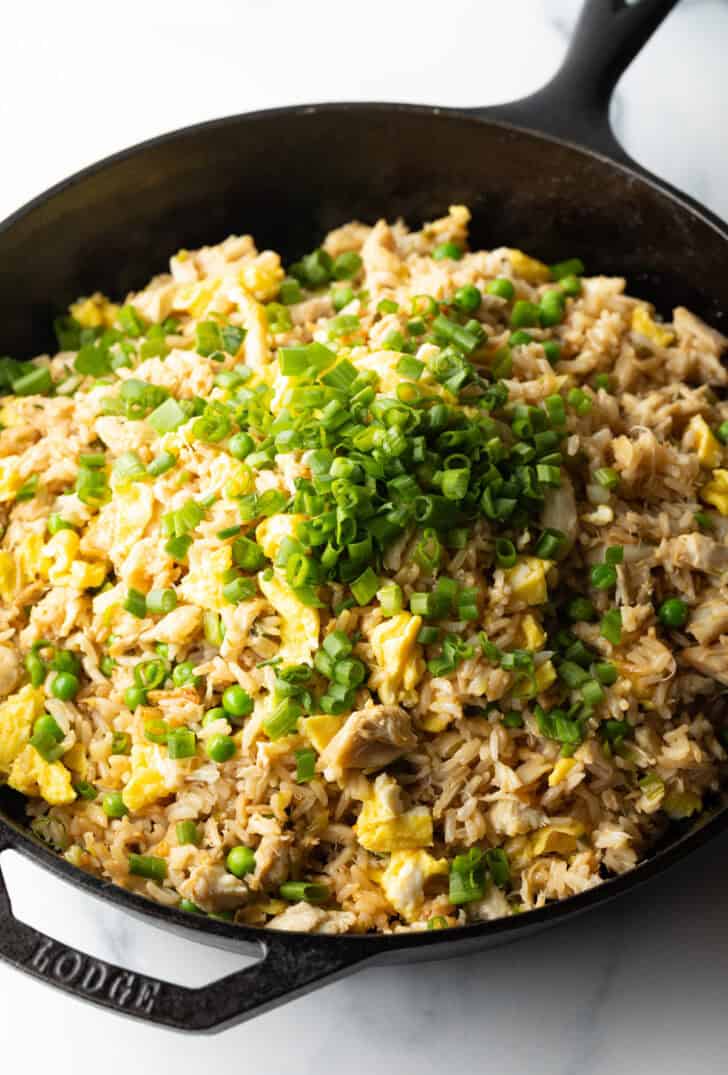 Adding green scallions to a skillet of crab meat and fried rice.