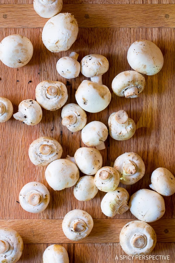 Cutting board covered with white button mushrooms for sauteed mushrooms
