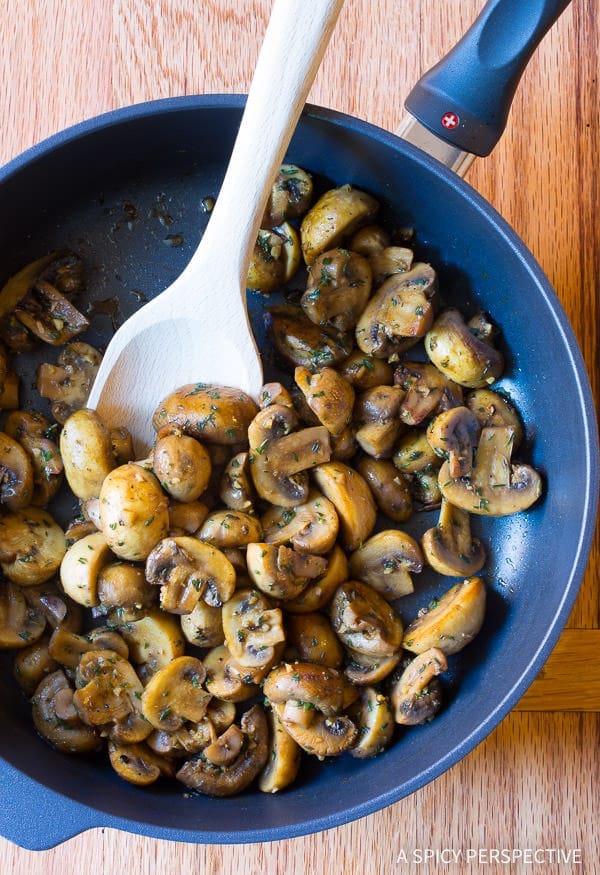 Wooden spoon stirring up the mushrooms in a skillet after being cooked. 
