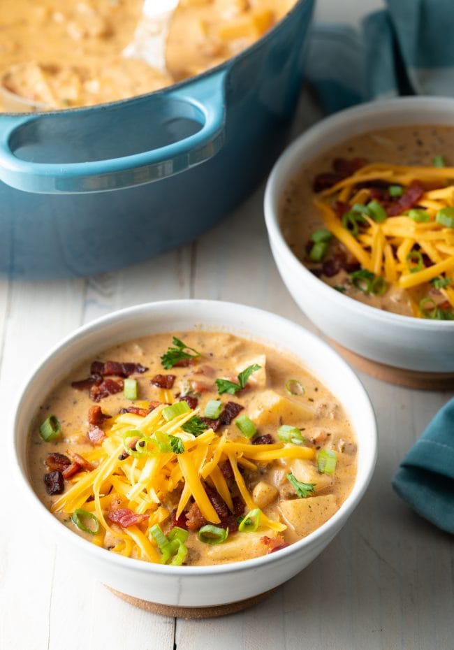 Bacon Cheeseburger Soup served in a white bowl and topped with bacon bites, cheese and green onions. 