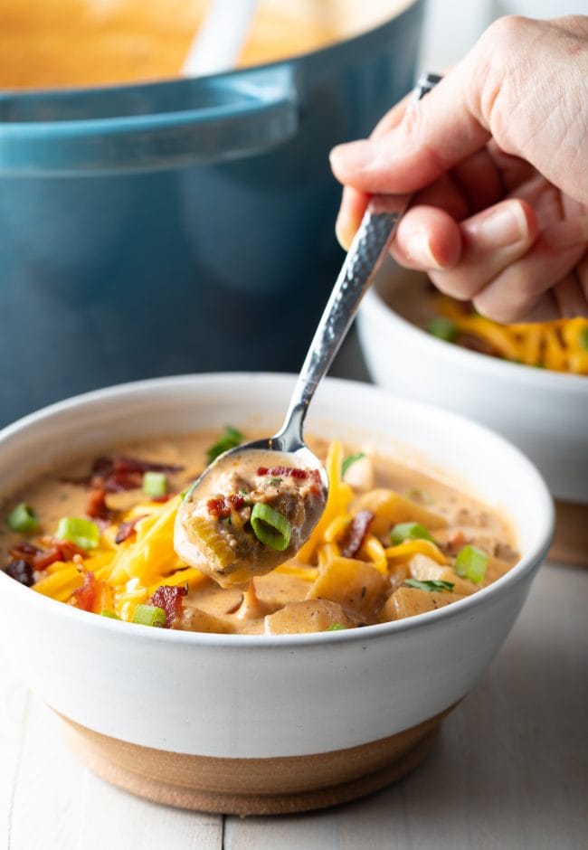 Hand taking a scoop of cheeseburger soup with a spoon. 