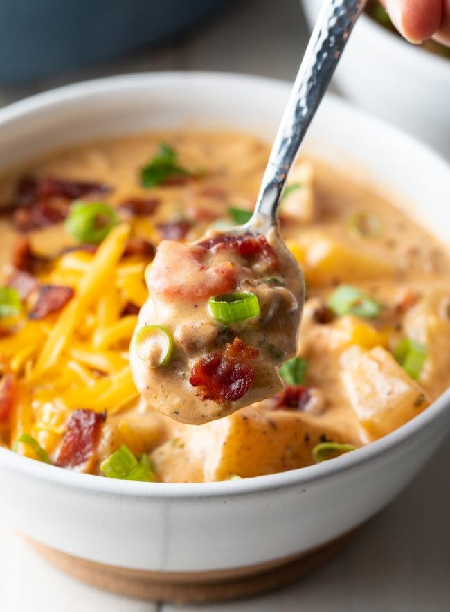 Easy cheeseburger soup with bacon in bowl with a spoon scooping up a bite. 