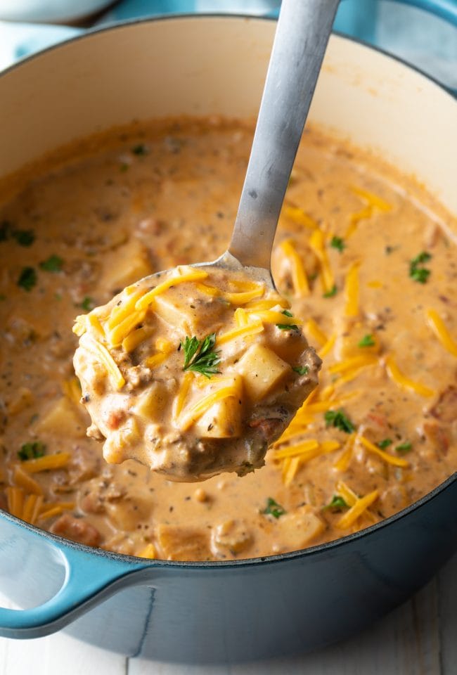 Ladle scooping up a serving of cheeseburger soup from the pot. 