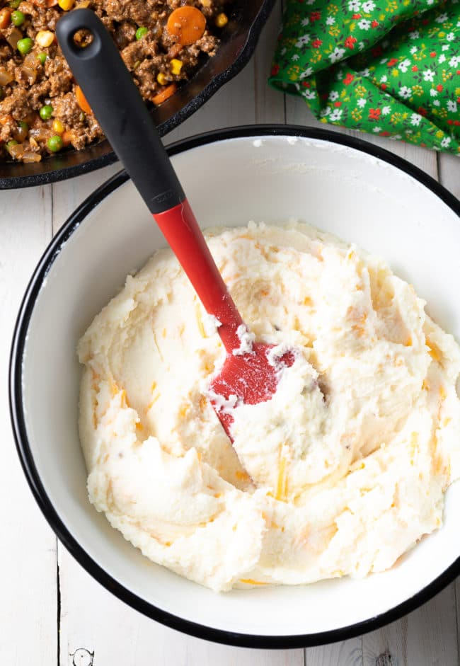 Mashed potatoes being mixed with cheese in a mixing bowl. 