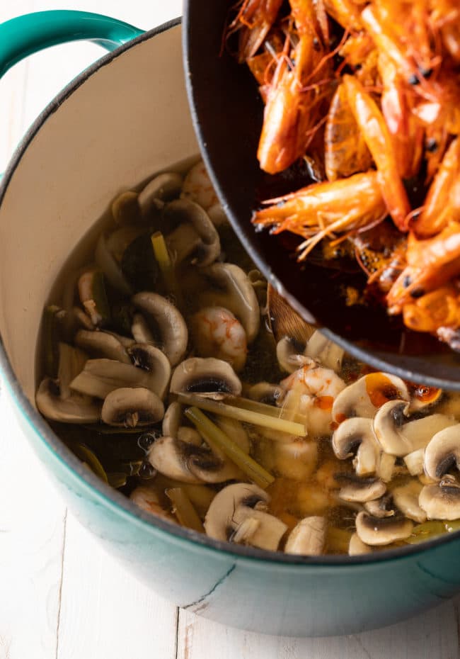 Adding shrimp oil to the soup in a dutch oven. 