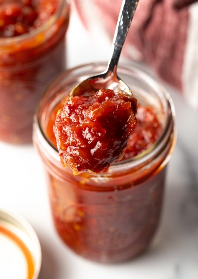 Tomato jam in a jar with a spoon scooping up some jam. 