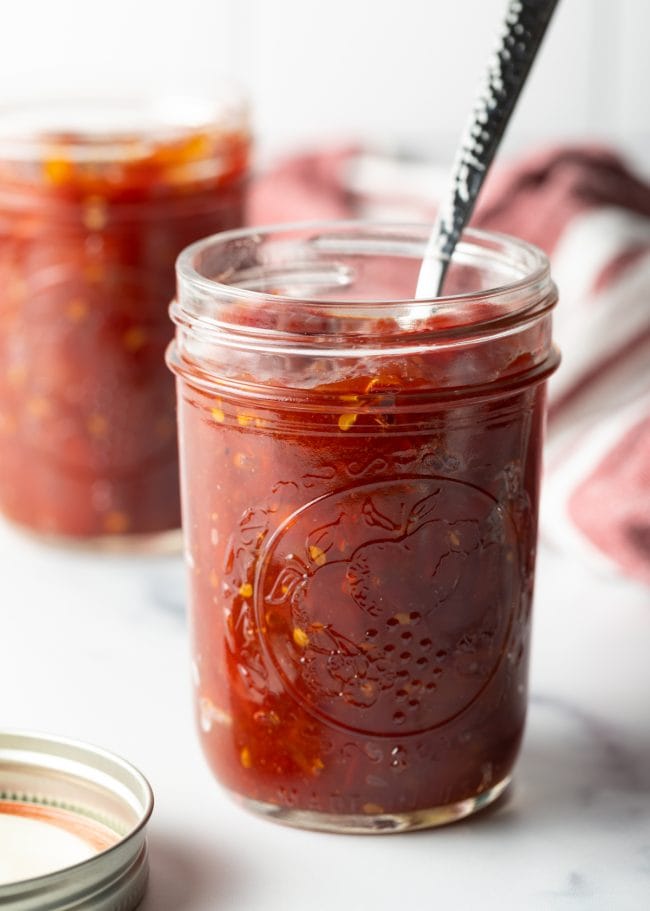 Full jar of homemade tomato jam with spoon in it.