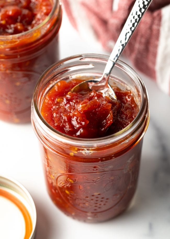 Spooning out a scoop of tomato jam from a mason jar.