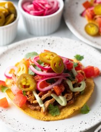 Close view chicken tinga tostada loaded with pickled veggies.