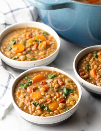 3 white bowls of lentil soup with carrots and kale.