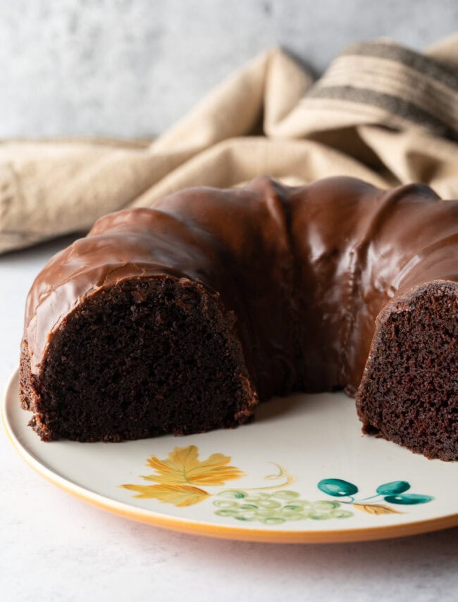 Triple chocolate Bundt cake with thick chocolate glaze. Segments of the cake have been removed to show the inside crumb of the cake.