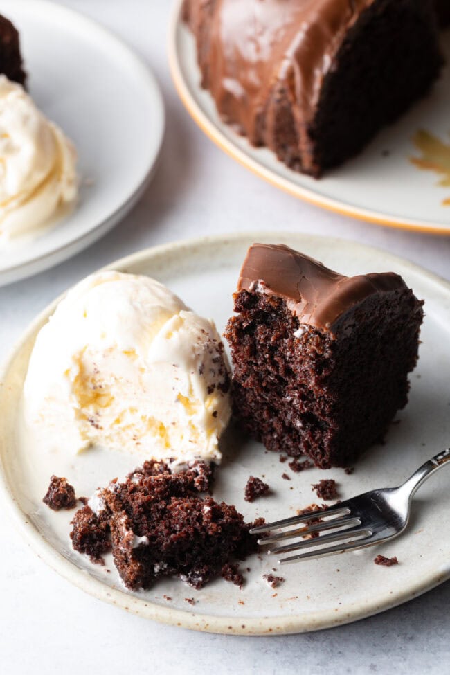 Slice of chocolate glazed cake on a white plate, with serving of vanilla ice cream and fork on the plate.