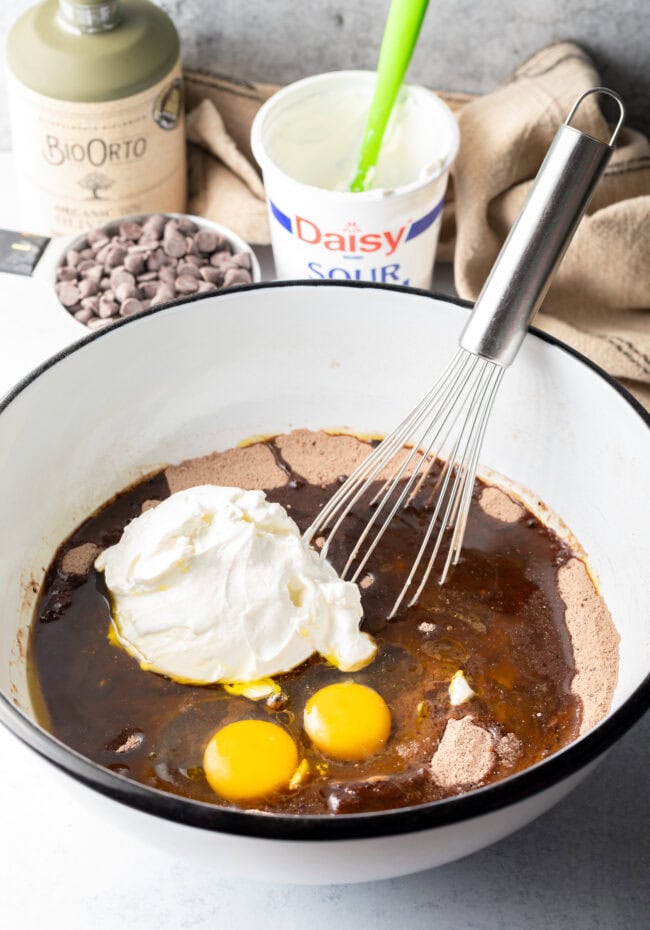 Adding eggs and sour cream to the white mixing bowl.