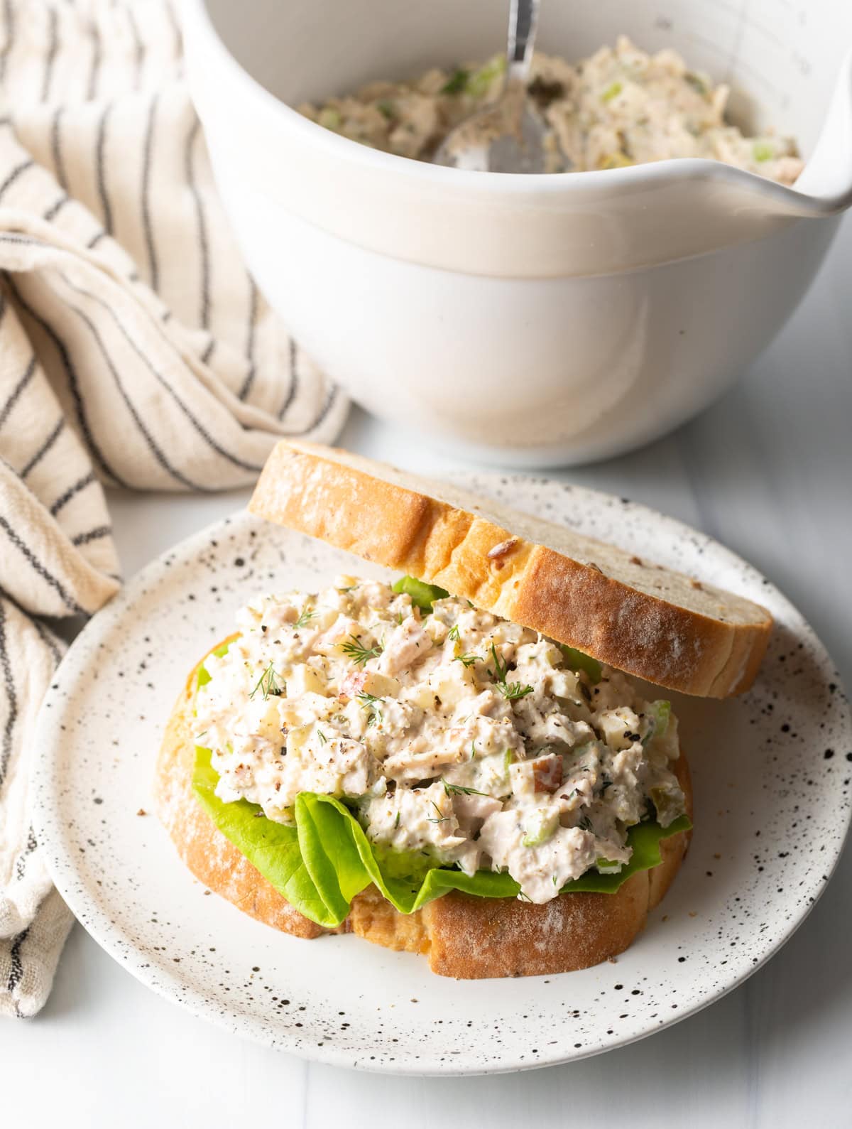 side view of bowl with salad and homemade tuna sandwich on a white plate.