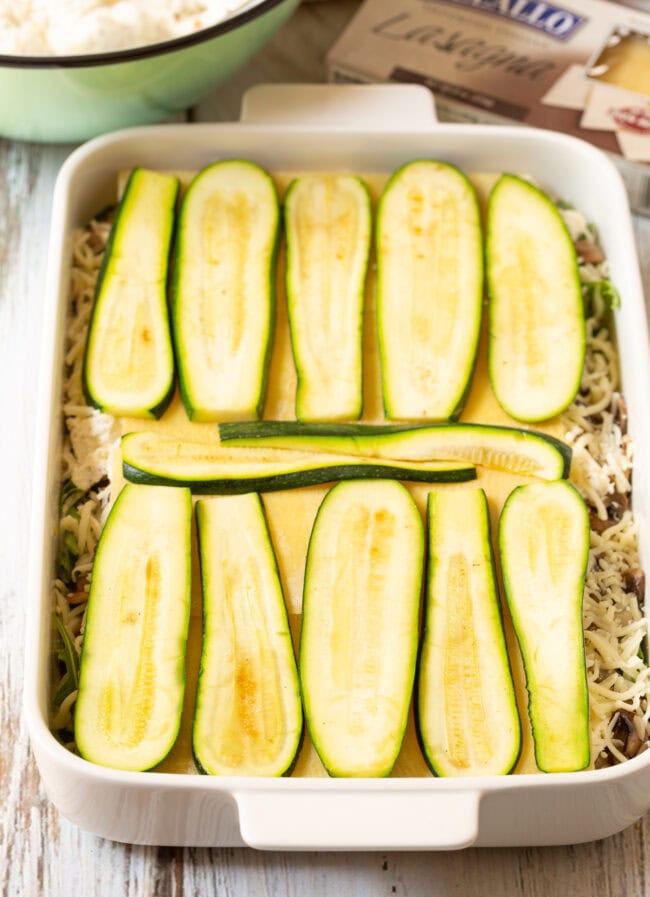 White baking dish with layers of lasagna. Top layer is thinly sliced zucchini. 