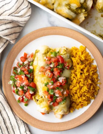 Top down view white plate with a serving of veggie enchiladas with green sauce and pico de gallo, nestled between a serving of pico de gallo and spanish rice.