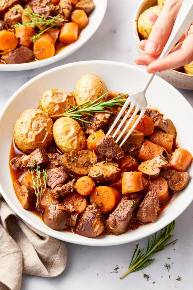 Venison Stew Recipe in a white bowl with a side of potatoes. 