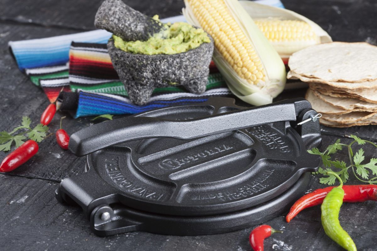 Victoria cookware tortilla press next to chili peppers, cork, and tortillas. 