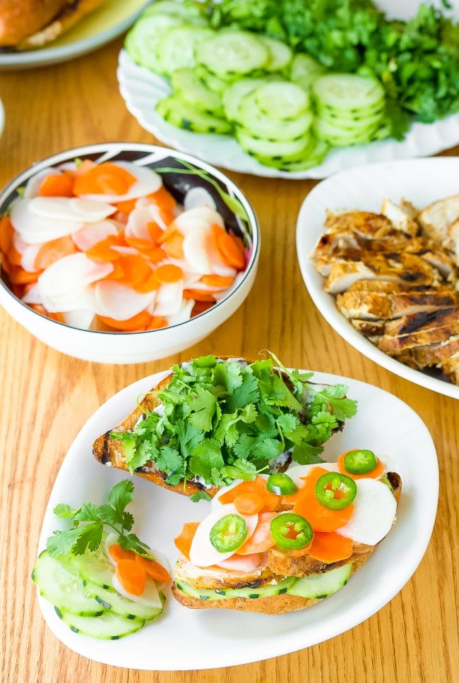 Vietnamese banh mi recipe - sandwiches on plates piled with vegetables and herbs