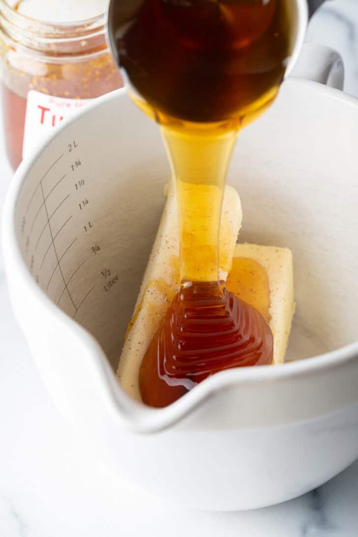 Pouring honey over two sticks of softened butter in a large mixing pitcher.