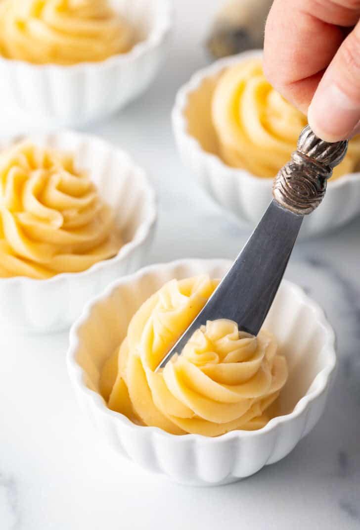 Butter knife cutting into a swirl of whipped honey butter in a ramekin.