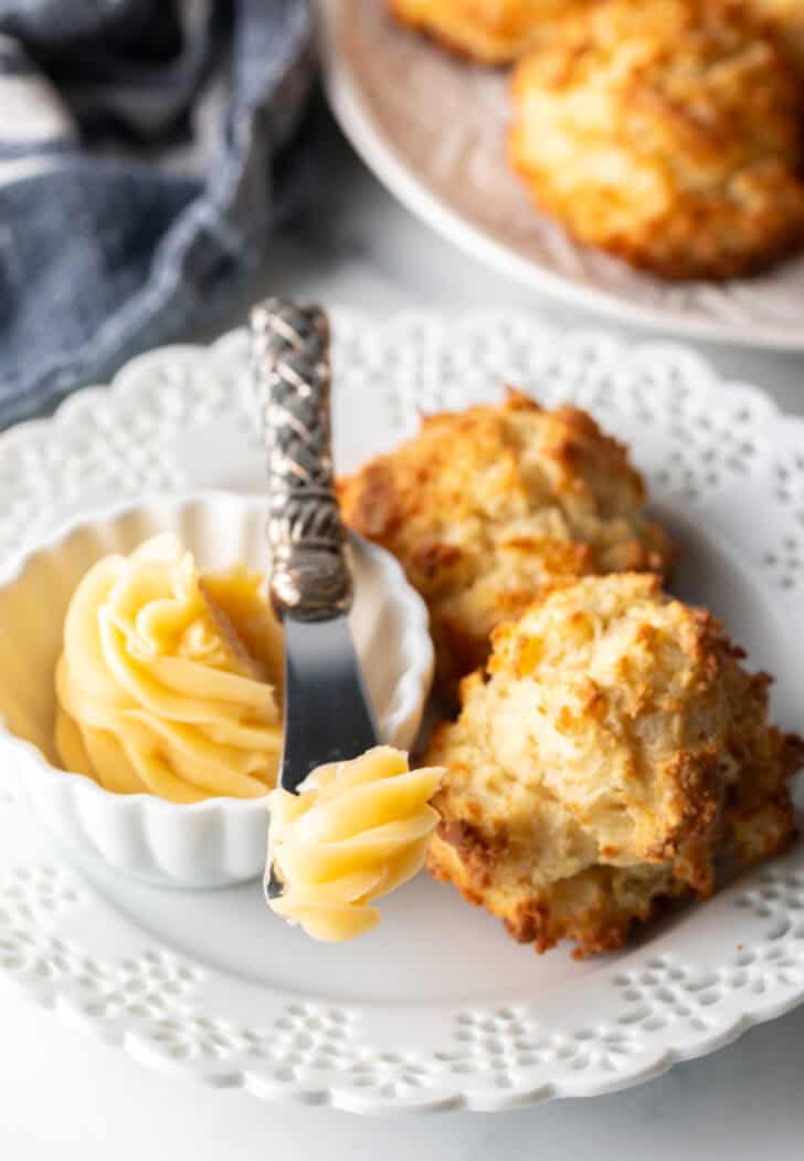 White plate with two drop biscuits, white ramekin of honey butter with a small knife.