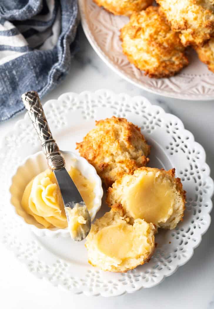 White plate with two drop biscuits, white ramekin of honey butter with a small knife.