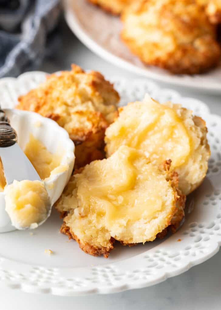 Soft drop biscuit split in half on a white plate, each half smeared with whipped honey butter.