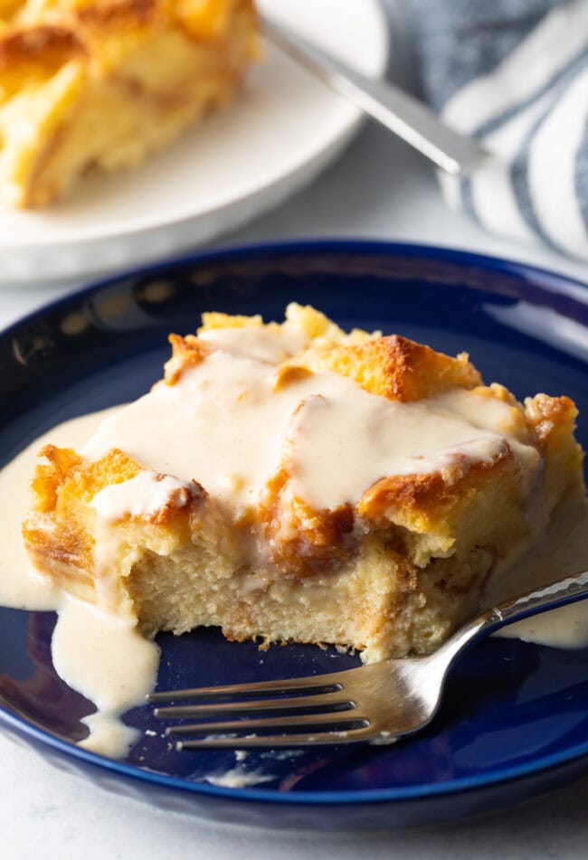 Slice of bread pudding on a plate with bite removed by fork.