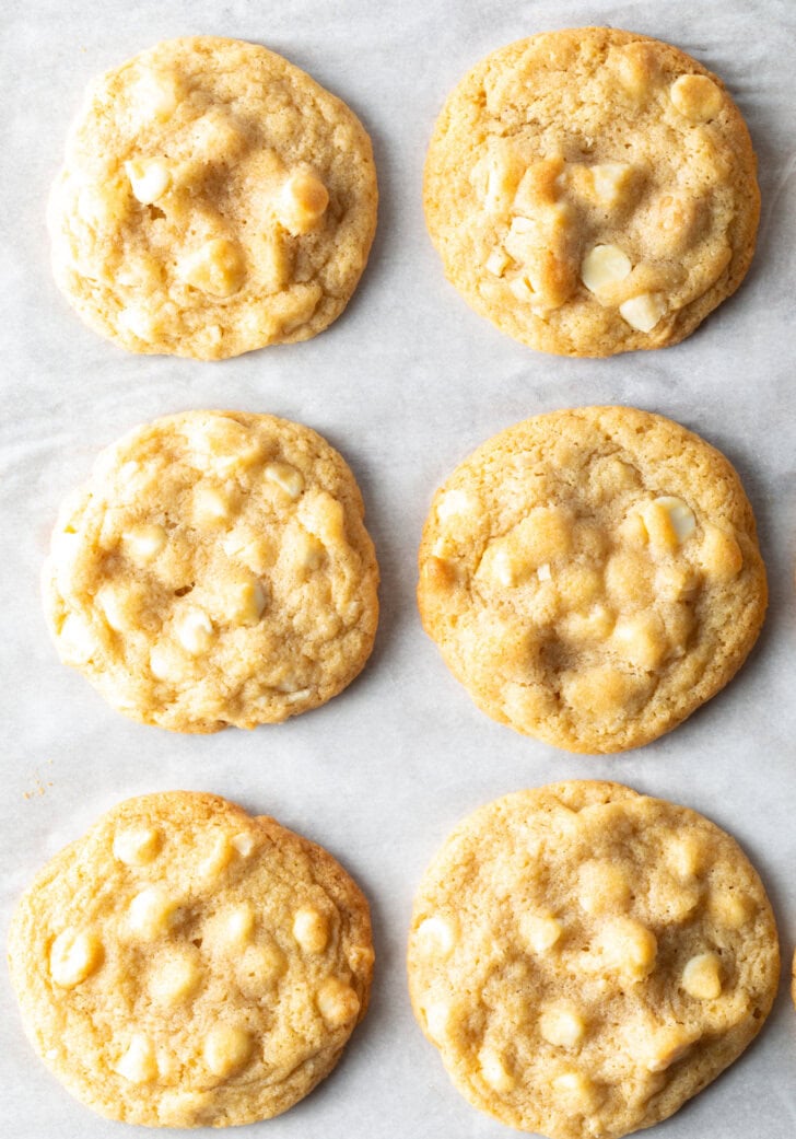 Three rows of three each white chocolate macadamia nut cookies on parchment.