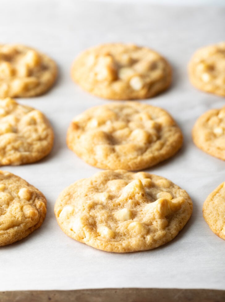 Three rows of three each white chocolate macadamia nut cookies on parchment.