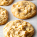 Close up view of three white chocolate macadamia nut cookies on parchment.